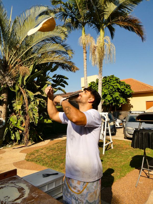 לירון מעיף בצק פיצה באוויר בחצר, ליד העמדה