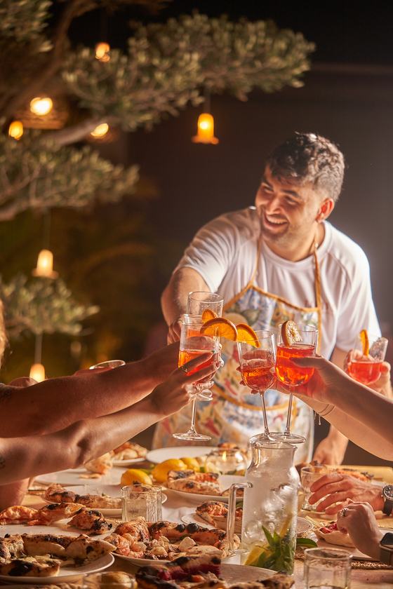 מארח עם סינר מרים כוסית עם האורחים ליד שולחן ערוך באירוע ערב